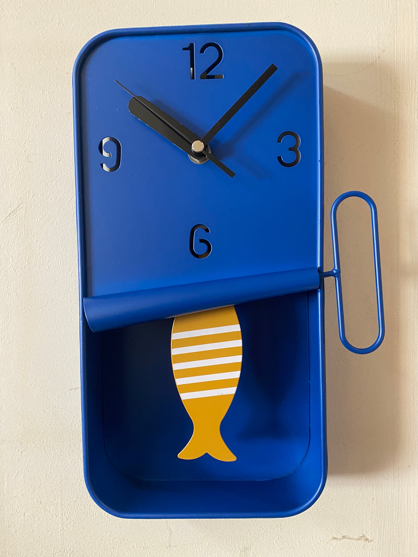 Blue clock-shaped container with a yellow fish design on a beige background