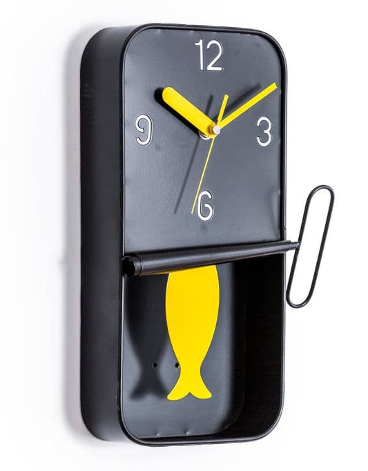 A black metal wall clock designed to resemble a sardine tin with a yellow pendulum.