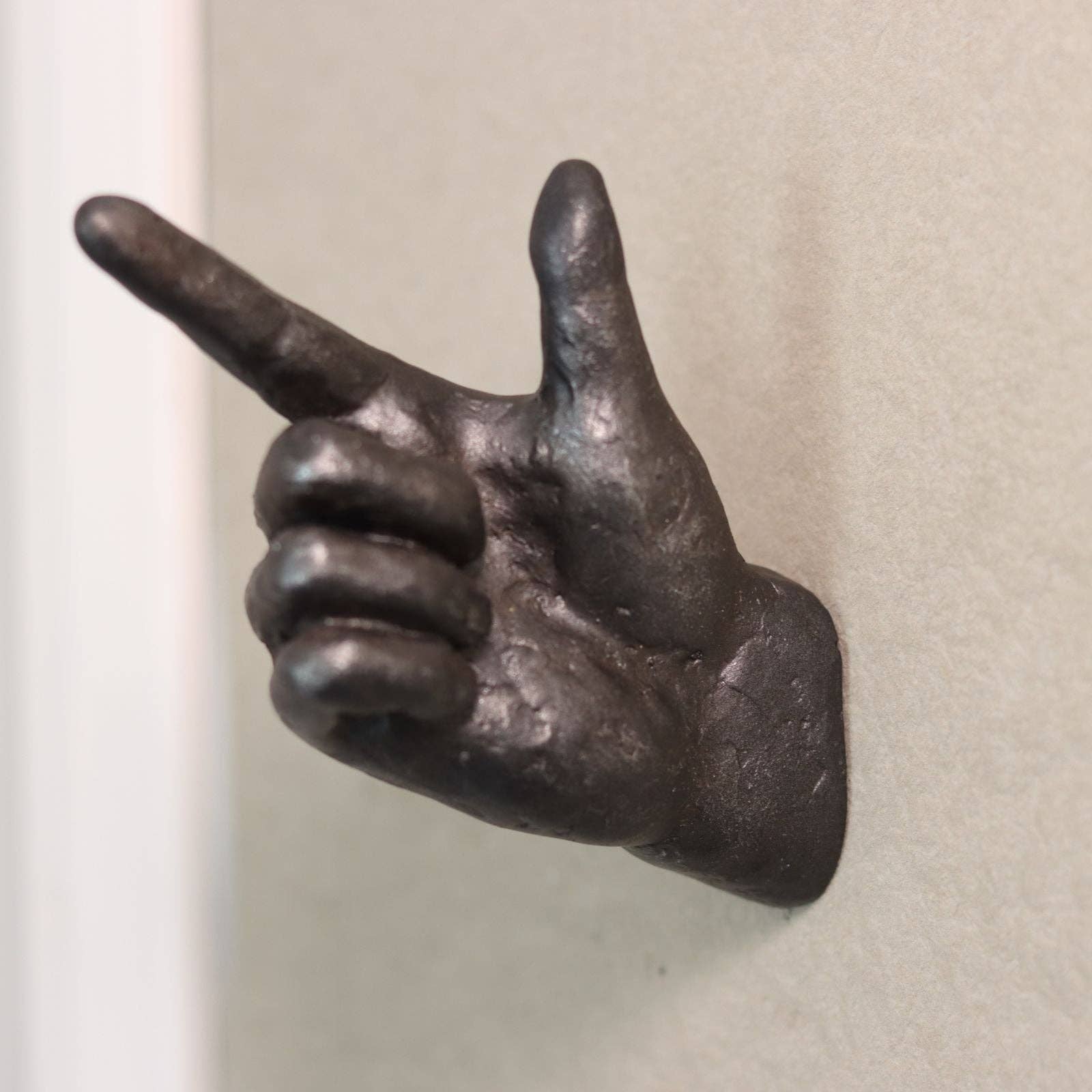 Bronze hand sculpture making a peace sign on a plain background