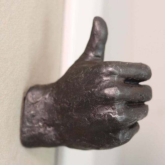 Bronze hand sculpture giving a thumbs-up gesture on a plain background